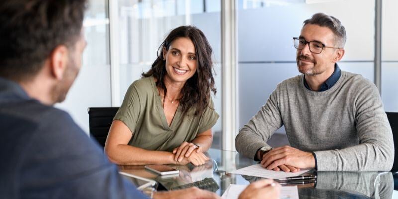 A man and a woman smiling in a meeting with their financial advisor.