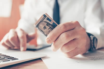 man and laptop holding dollar bills