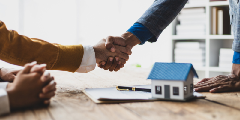 Mortgage advisor shaking hands with client across a table.